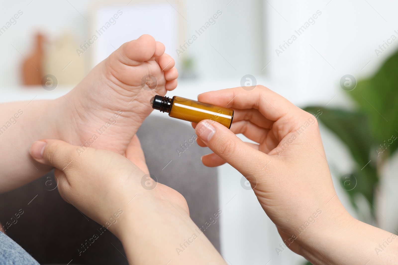 Photo of Mother applying essential oil from roller bottle onto her baby`s heel indoors, closeup