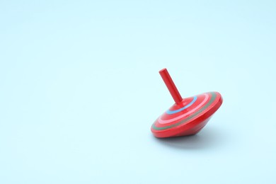 Photo of One bright spinning top on light blue background, space for text. Toy whirligig