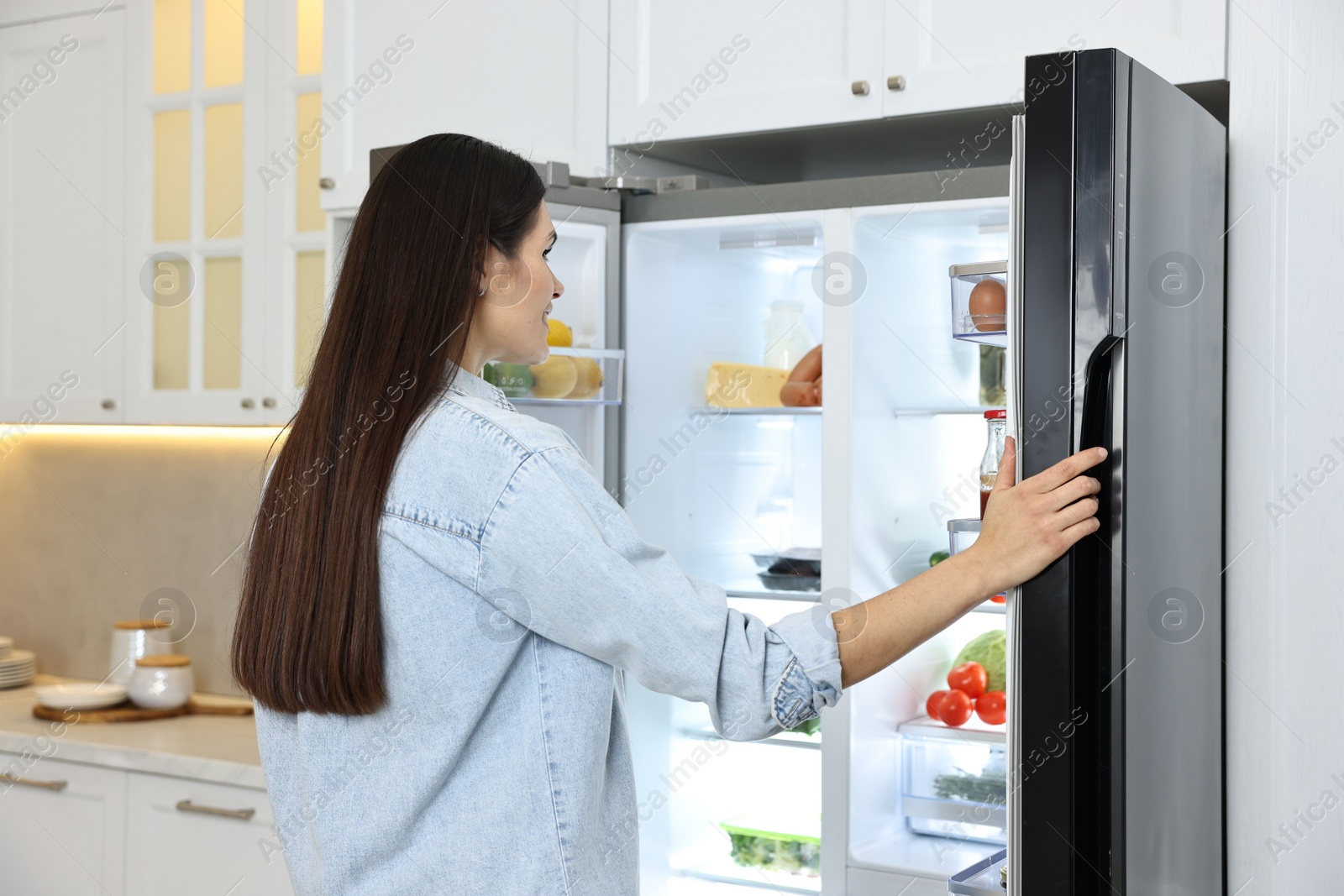 Photo of Young woman near modern refrigerator in kitchen