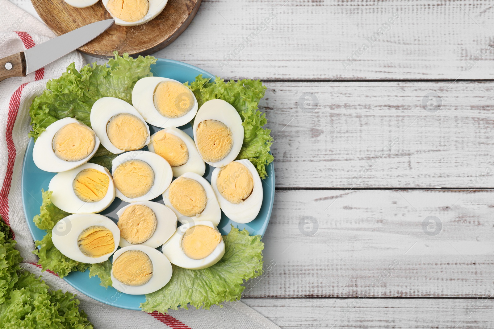 Photo of Fresh hard boiled eggs and lettuce on white wooden table, top view. Space for text