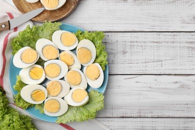 Fresh hard boiled eggs and lettuce on white wooden table, top view. Space for text