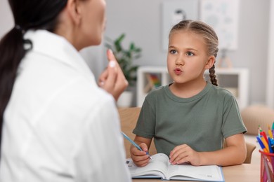 Photo of Dyslexia treatment. Speech therapist working with girl at table in room