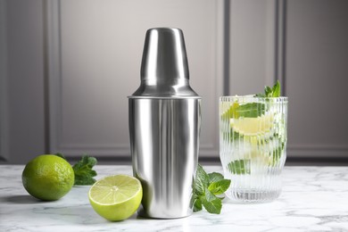 Photo of Metal cocktail shaker, delicious mojito, limes and mint on white marble table