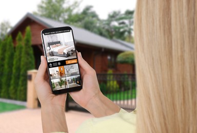 Woman using smart home security system on mobile phone near house outdoors. Device showing different rooms through cameras
