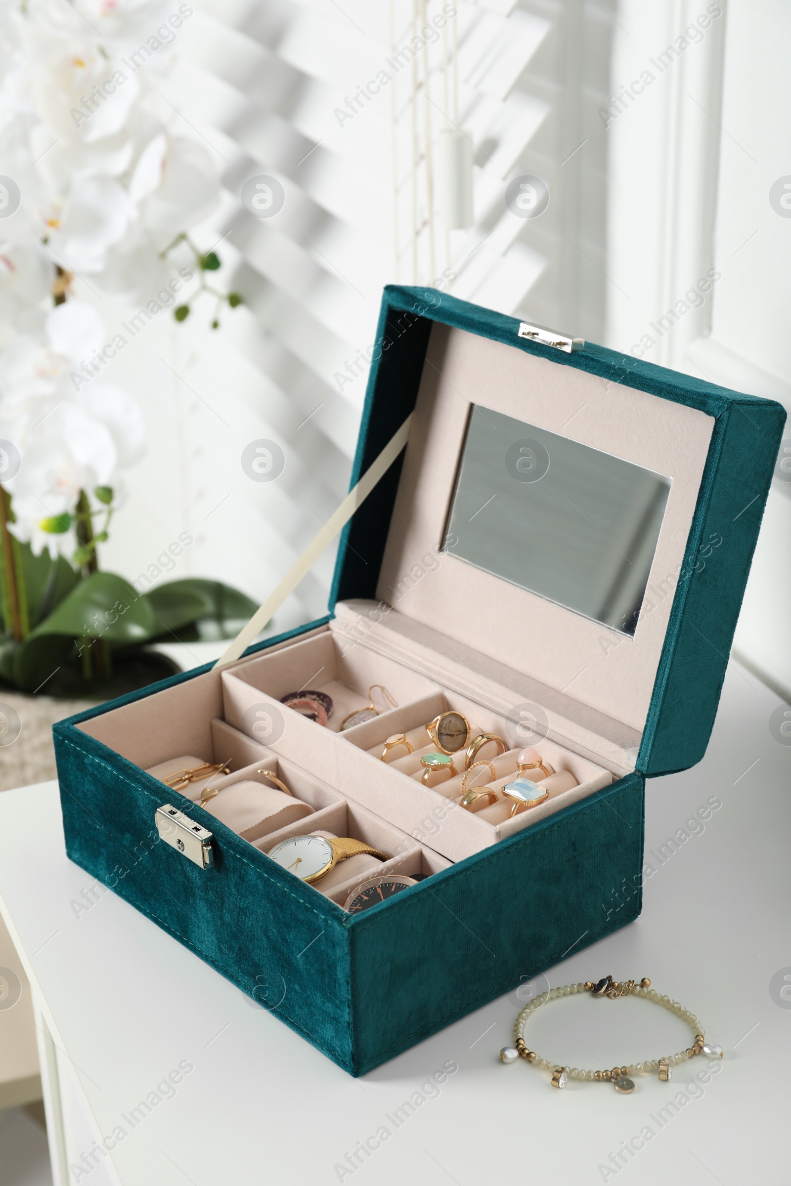 Photo of Elegant jewelry box with beautiful bijouterie and expensive wristwatches on white table in room