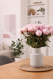 Photo of Vase with pink peonies on wooden table in dining room