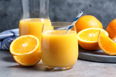 Photo of Glass of orange juice and fresh fruits on grey table, closeup