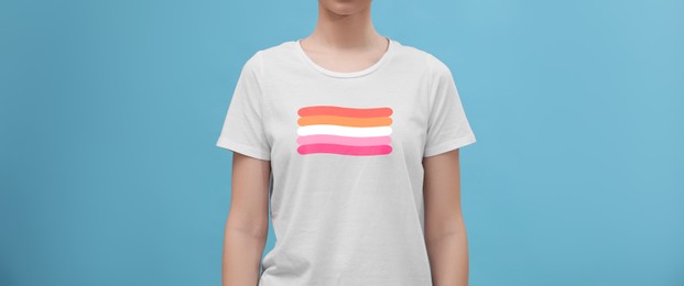 Image of Young woman wearing white t-shirt with lesbian flag on light blue background, banner design. LGBT concept