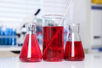 Photo of Laboratory analysis. Different glassware with red liquid on white table indoors