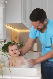 Father washing his little baby in sink at home