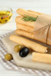 Photo of Tasty grissini with rosemary, olives and oil on white wooden table, closeup