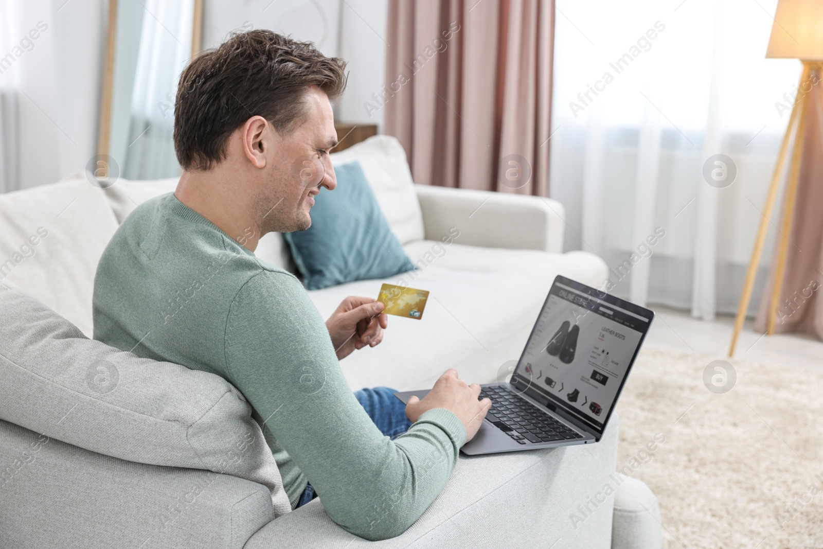 Photo of Man with credit card and laptop shopping online on sofa at home