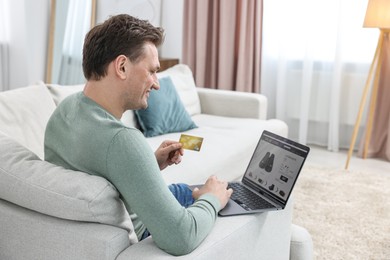 Photo of Man with credit card and laptop shopping online on sofa at home