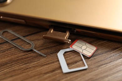 Photo of SIM card, mobile phone and ejector tool on wooden table, closeup