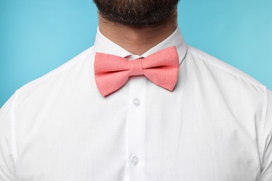 Man in shirt and bow tie on light blue background, closeup