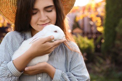 Happy woman holding cute rabbit outdoors on sunny day, closeup. Space for text
