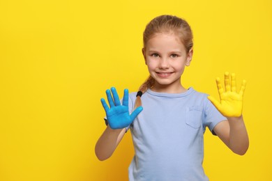 Photo of Little girl with hands painted in Ukrainian flag colors on yellow background, space for text. Love Ukraine concept