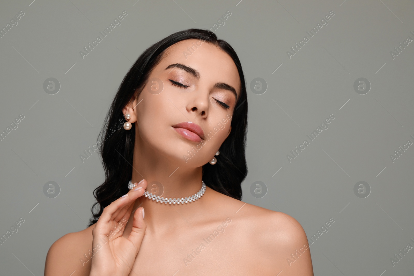 Photo of Young woman wearing elegant pearl jewelry on grey background, space for text