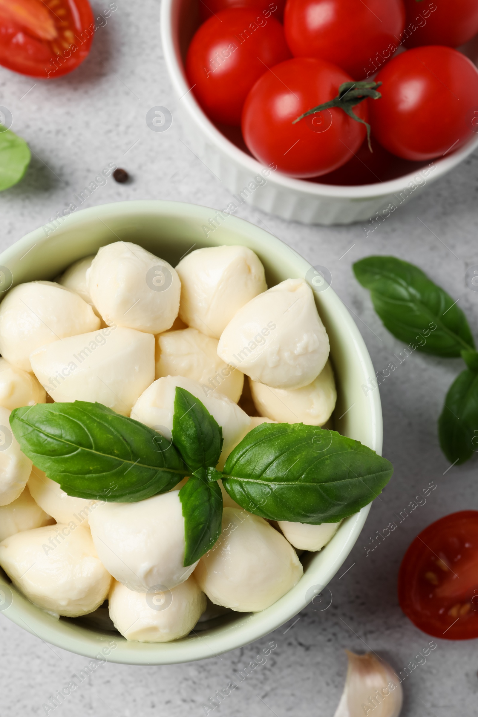 Photo of Delicious mozzarella balls in bowl, tomatoes and basil leaves on light gray table, flat lay