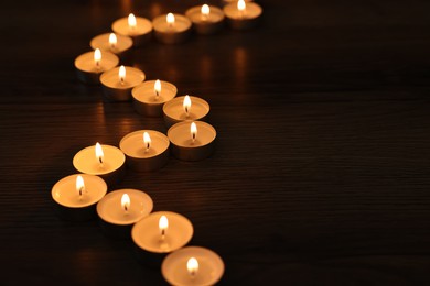 Photo of Burning candles on wooden table in darkness, space for text