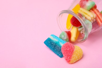 Photo of Tasty jelly candies and jar on pink background. Space for text