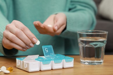 Photo of Woman taking pill from plastic box at wooden table indoors, closeup