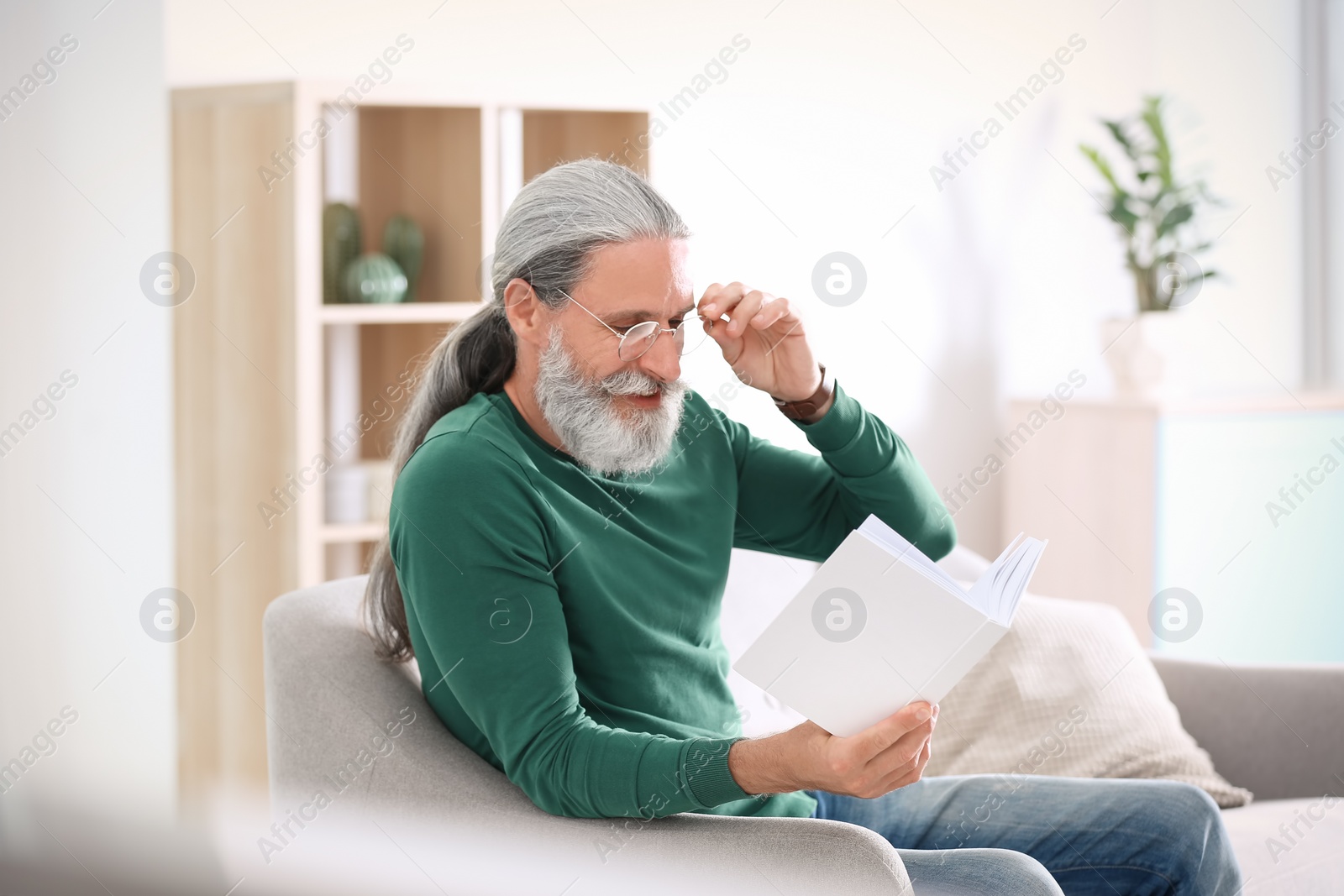 Photo of Handsome mature man reading book on sofa, indoors