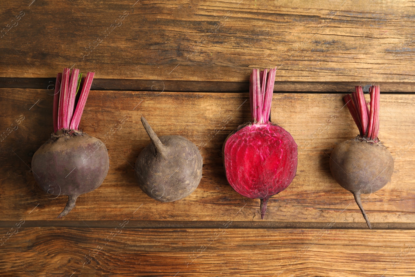 Photo of Cut and whole raw beets on wooden table, flat lay