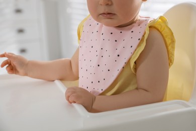 Photo of Cute little baby wearing bib in highchair indoors, closeup