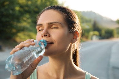 Photo of Happy young woman drinking water outdoors on hot summer day. Refreshing drink