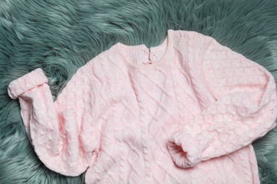 Photo of Pink knitted sweater on green fur rug, flat lay