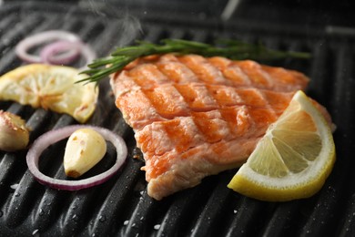Photo of Tasty salmon cooking with rosemary, garlic, onion and lemon on electric grill, closeup
