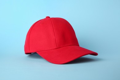 Photo of Stylish red baseball cap on light blue background