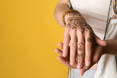 Photo of Woman with beautiful henna tattoo on hand against yellow background, closeup and space for text. Traditional mehndi