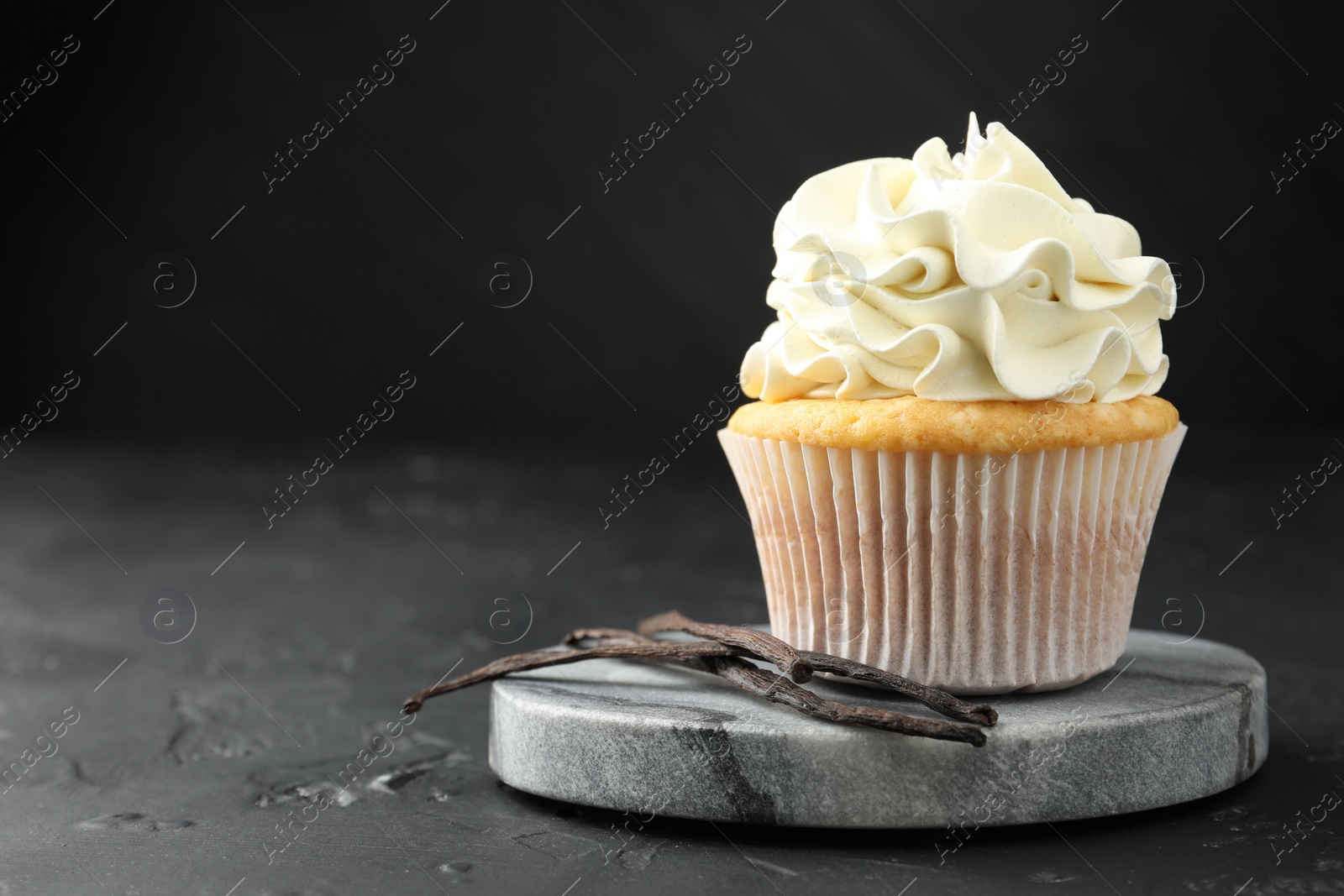 Photo of Tasty cupcake with cream and vanilla pods on black table, closeup. Space for text