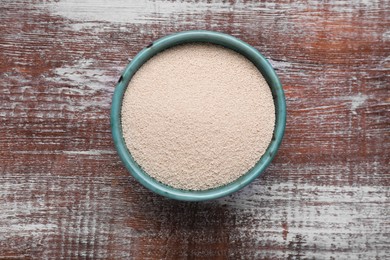 Photo of Bowl of active dry yeast on wooden table, top view