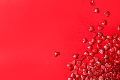 Photo of Bright heart shaped sprinkles on red background, flat lay. Space for text