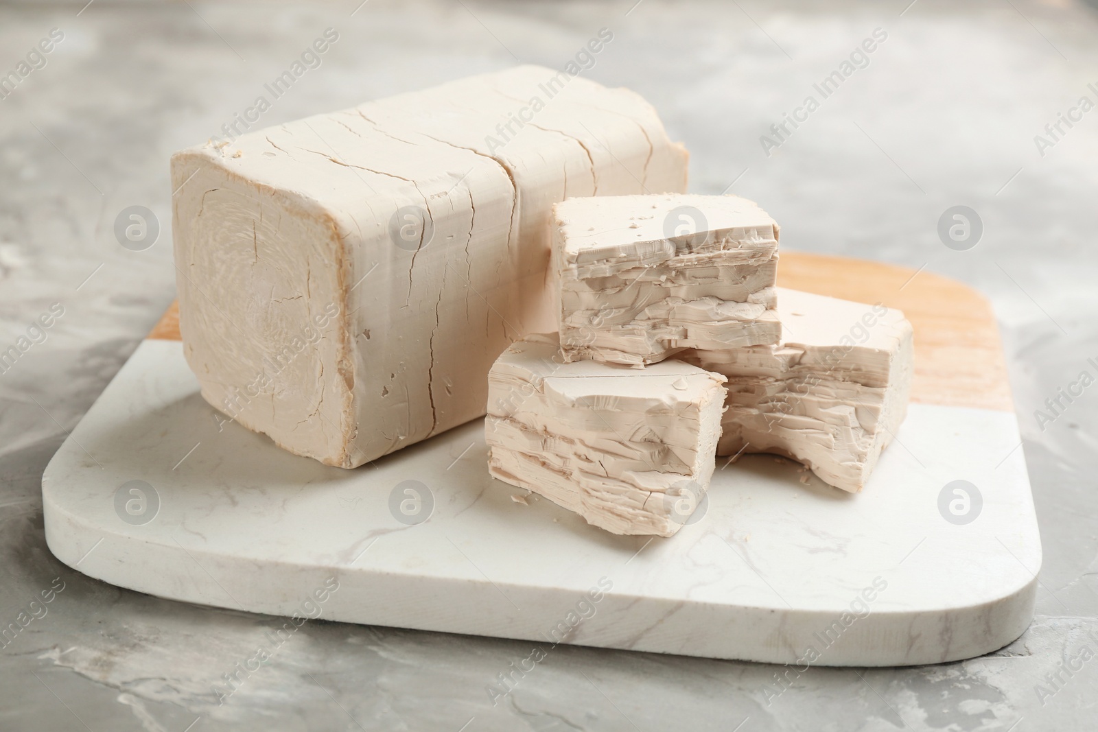 Photo of Board with pieces of compressed yeast on grey table