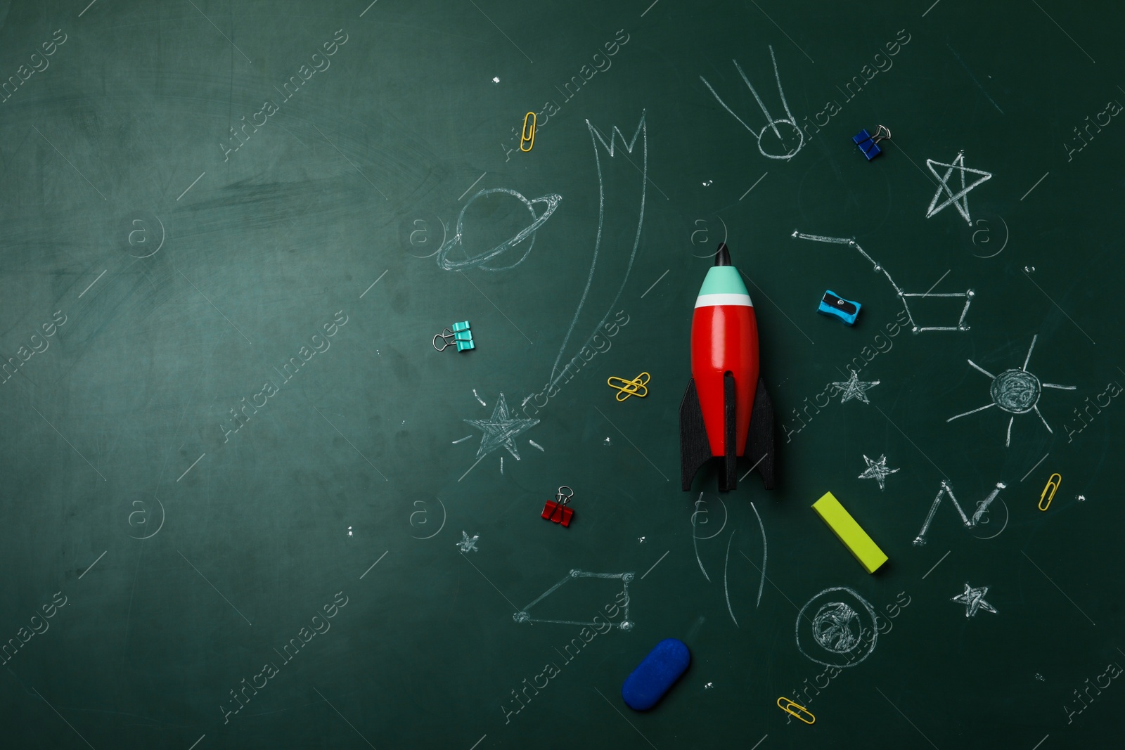 Photo of Bright toy rocket, school supplies and drawings on chalkboard, flat lay. Space for text