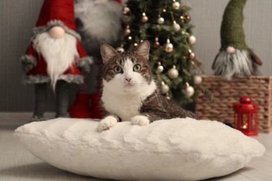 Photo of Cute cat lying on soft pillow near Christmas decor at home. Adorable pet