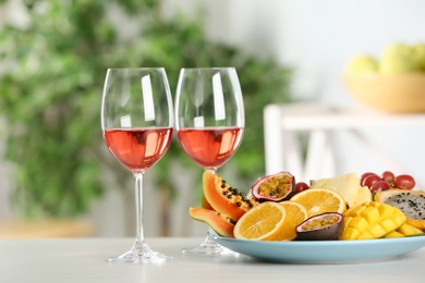 Delicious exotic fruits and glasses of wine on white table indoors