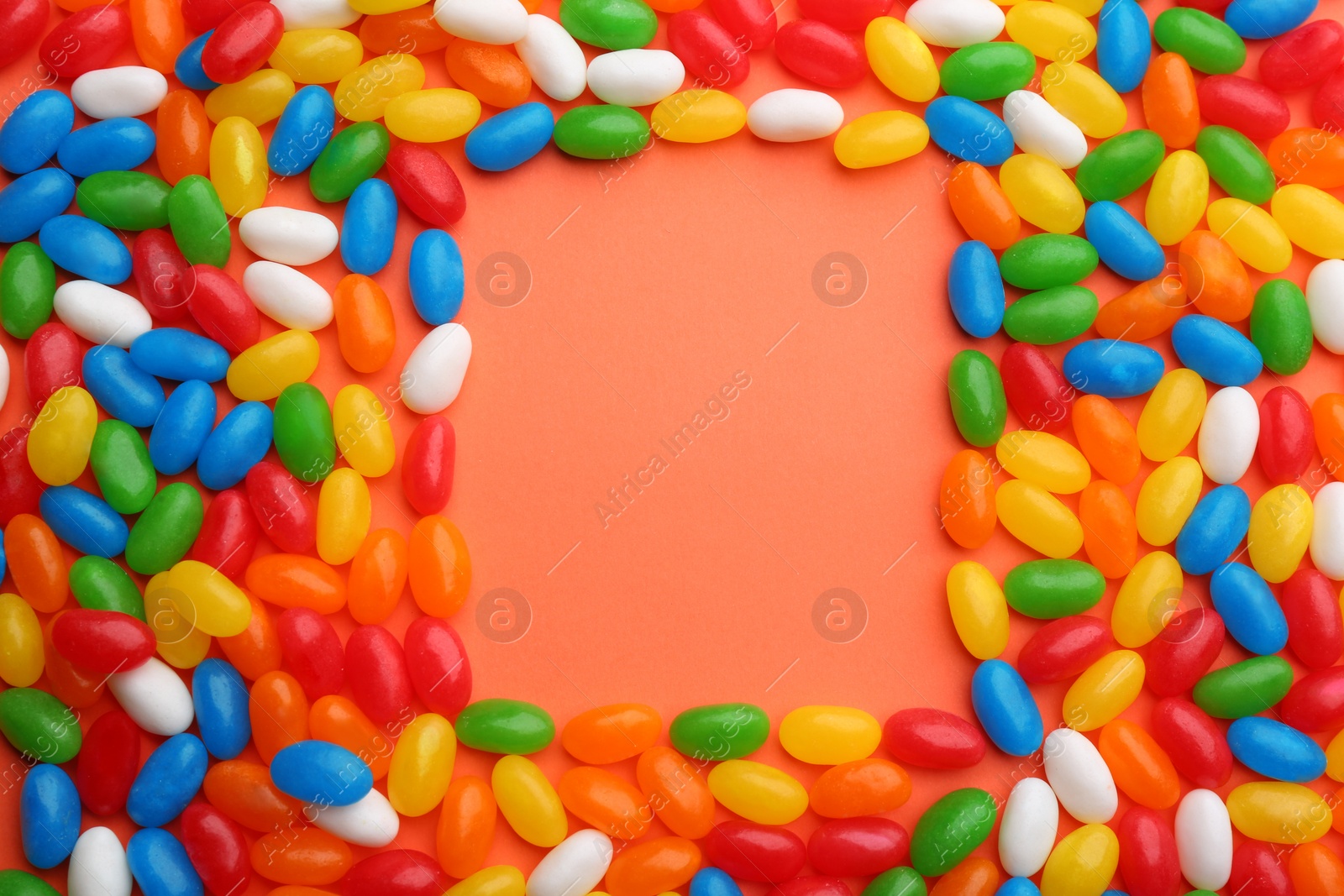 Photo of Frame made of colorful jelly beans on coral background, flat lay. Space for text