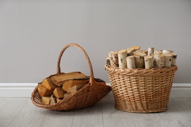 Wicker baskets with firewood near grey wall indoors