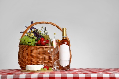 Photo of Picnic basket with wine and products on checkered tablecloth against white background. Space for text