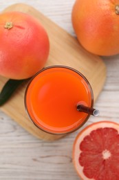 Photo of Tasty grapefruit juice in glass and fresh fruits on light wooden table, flat lay