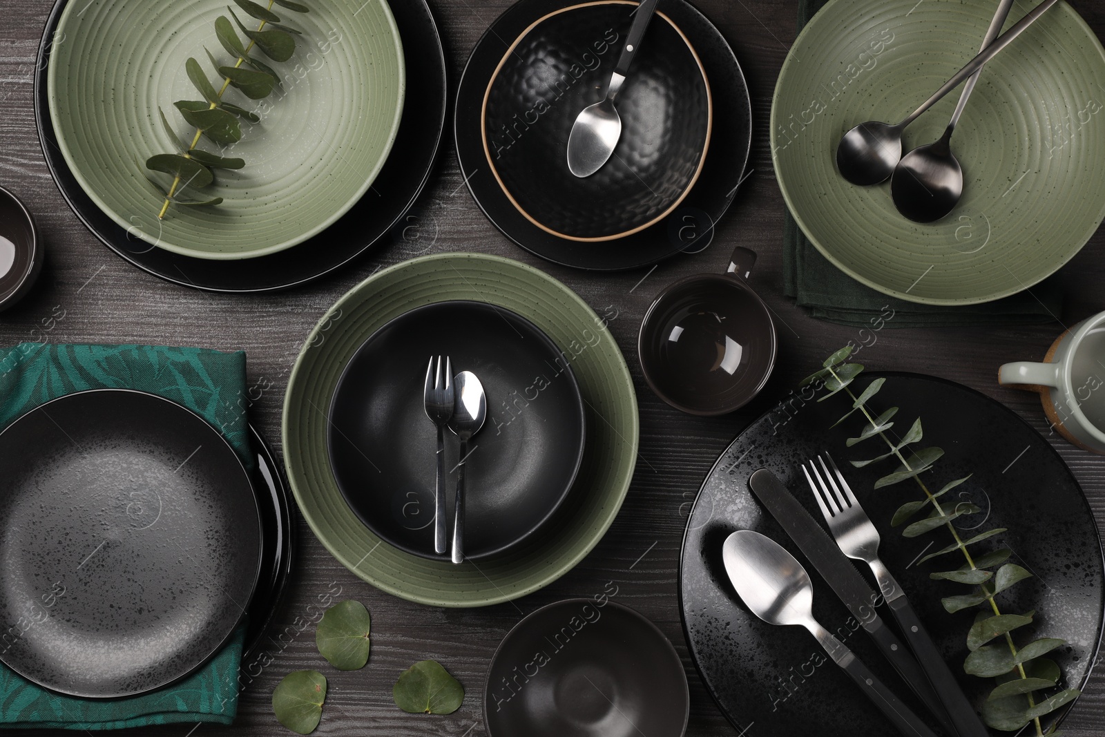 Photo of Stylish table setting with cutlery and eucalyptus branches on dark wooden background, flat lay