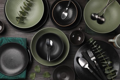 Stylish table setting with cutlery and eucalyptus branches on dark wooden background, flat lay