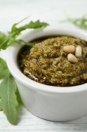 Photo of Bowl of tasty pesto and arugula on white wooden table