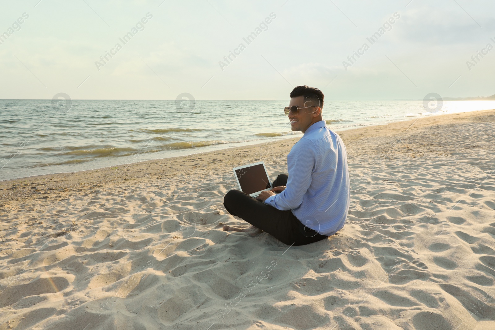 Photo of Happy businessman working with laptop on beach. Business trip