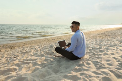 Happy businessman working with laptop on beach. Business trip